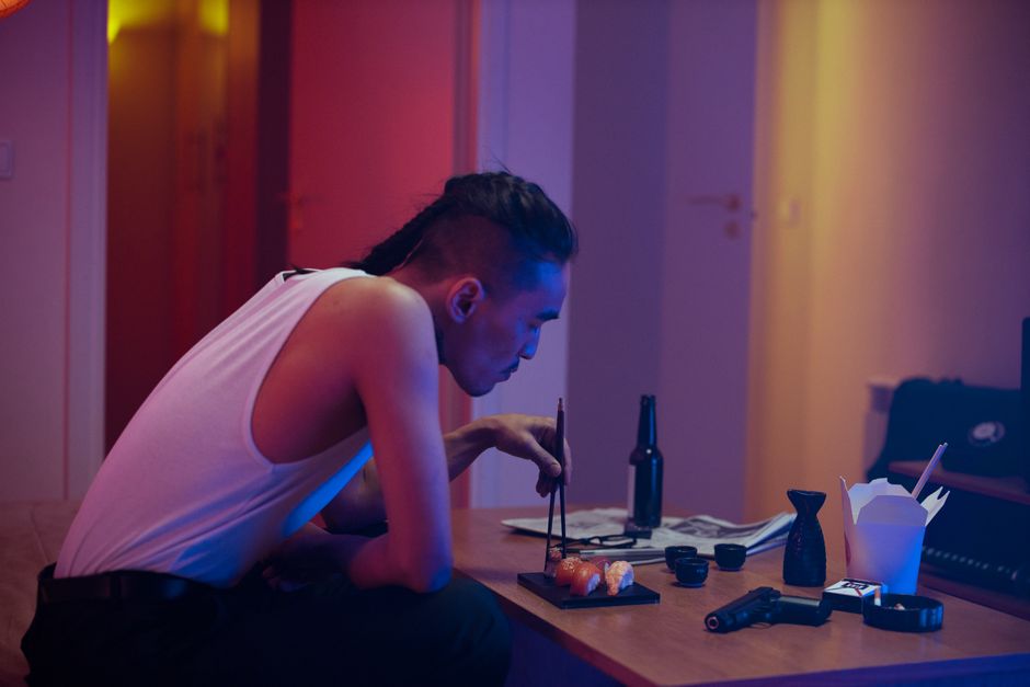 A man eating sushi with chopsticks indoors in a moody atmosphere.