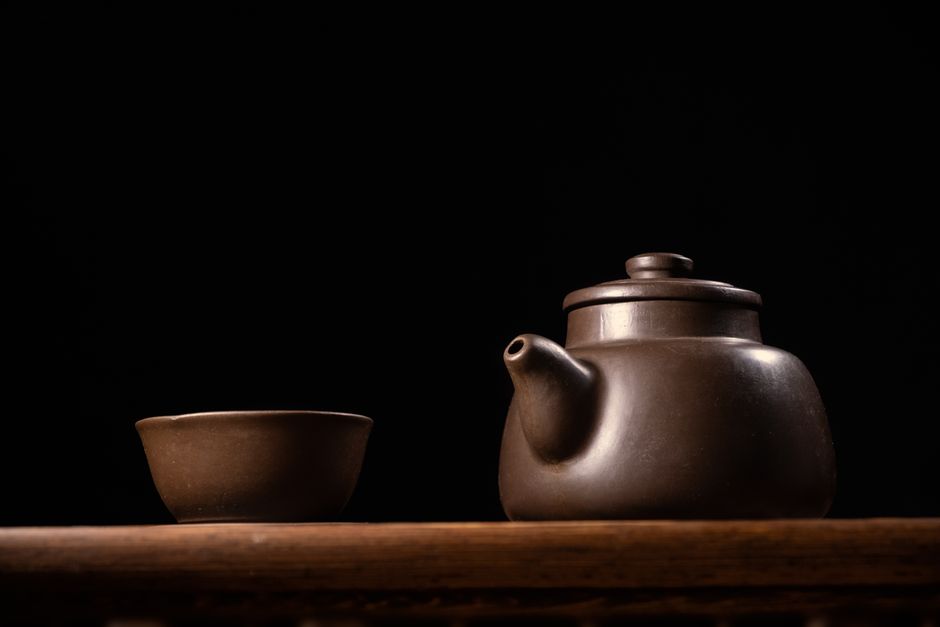 Minimalist still life of a Zisha teapot and cup against a dark background.