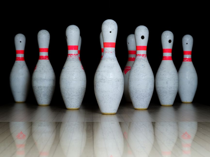 Nine bowling pins arranged with reflection in a bowling alley under dramatic lighting.