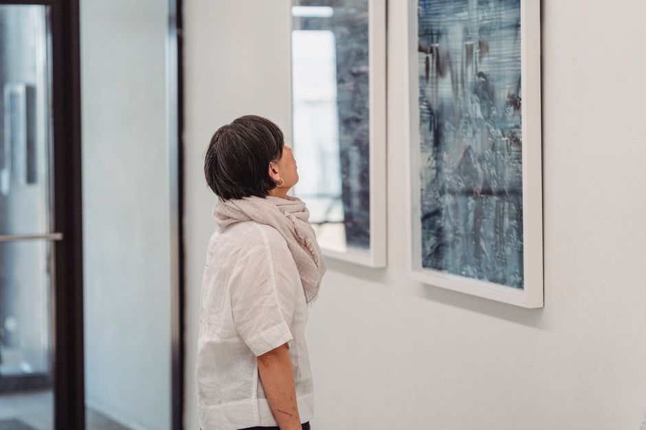 A woman in a gallery intently observes abstract paintings, highlighting her engagement with modern art.