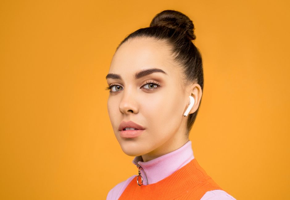 Stylish young woman with earphones, posing against a bright yellow background in a studio.