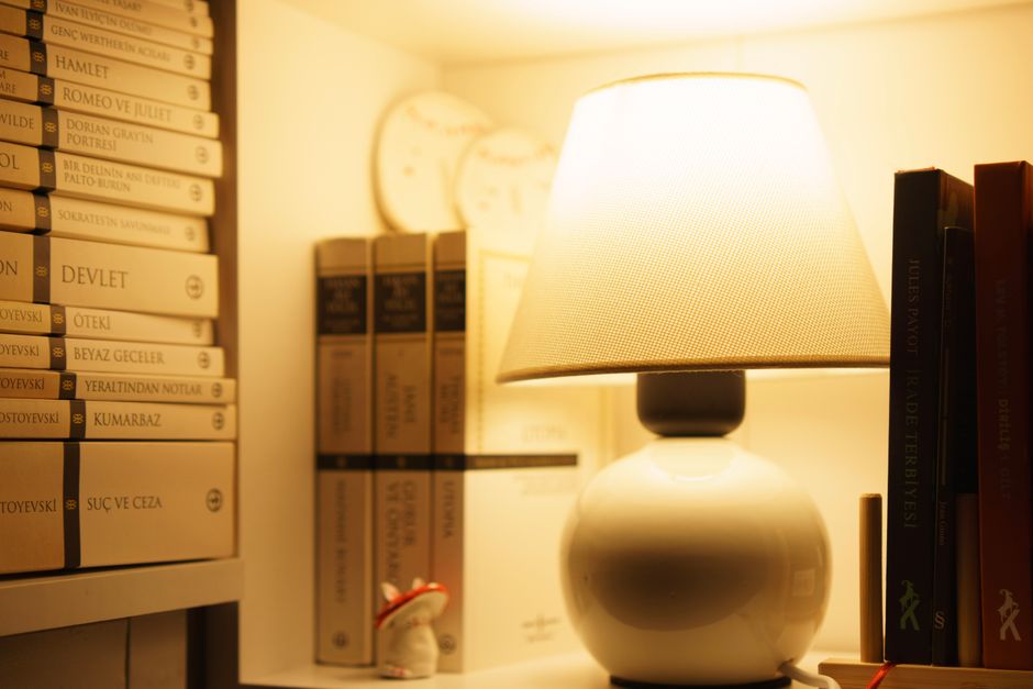 A warmly lit bookshelf with stacked books and an elegant table lamp, creating a cozy reading atmosphere.