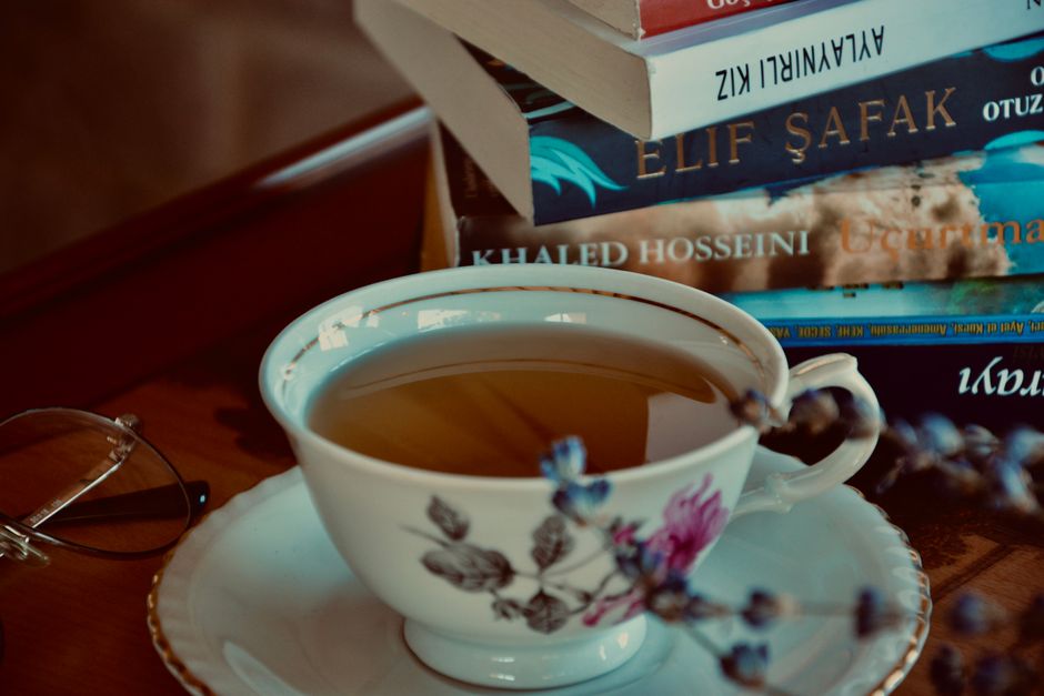 A cozy setup with a teacup, books, and glasses on a wooden table, perfect for a relaxing afternoon.